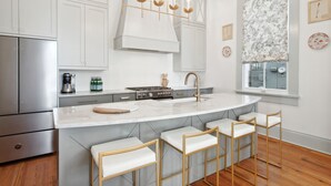 A modern kitchen with white cabinetry, a central island with bar stools, stainless steel appliances, and a decorative chandelier.