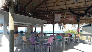 An outdoor bar area with tables and chairs, a thatched roof, and a view of the sea. - Sunset Lagoon. In the heart of Hudson. Waterfront. 2 minute walk beach/dining (Hudson)