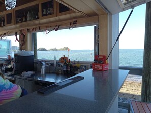 A bar area with a view of the sea, a counter with various items, and a shelf with bottles. - Sunset Lagoon. In the heart of Hudson. Waterfront. 2 minute walk beach/dining (Hudson)