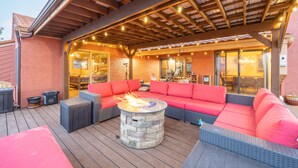 Un patio exterior con un hogar a leña de piedra, un sofá rojo y una zona cubierta con luces colgantes.