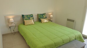 Una cama con una colcha verde, dos almohadas y dos lámparas de noche.