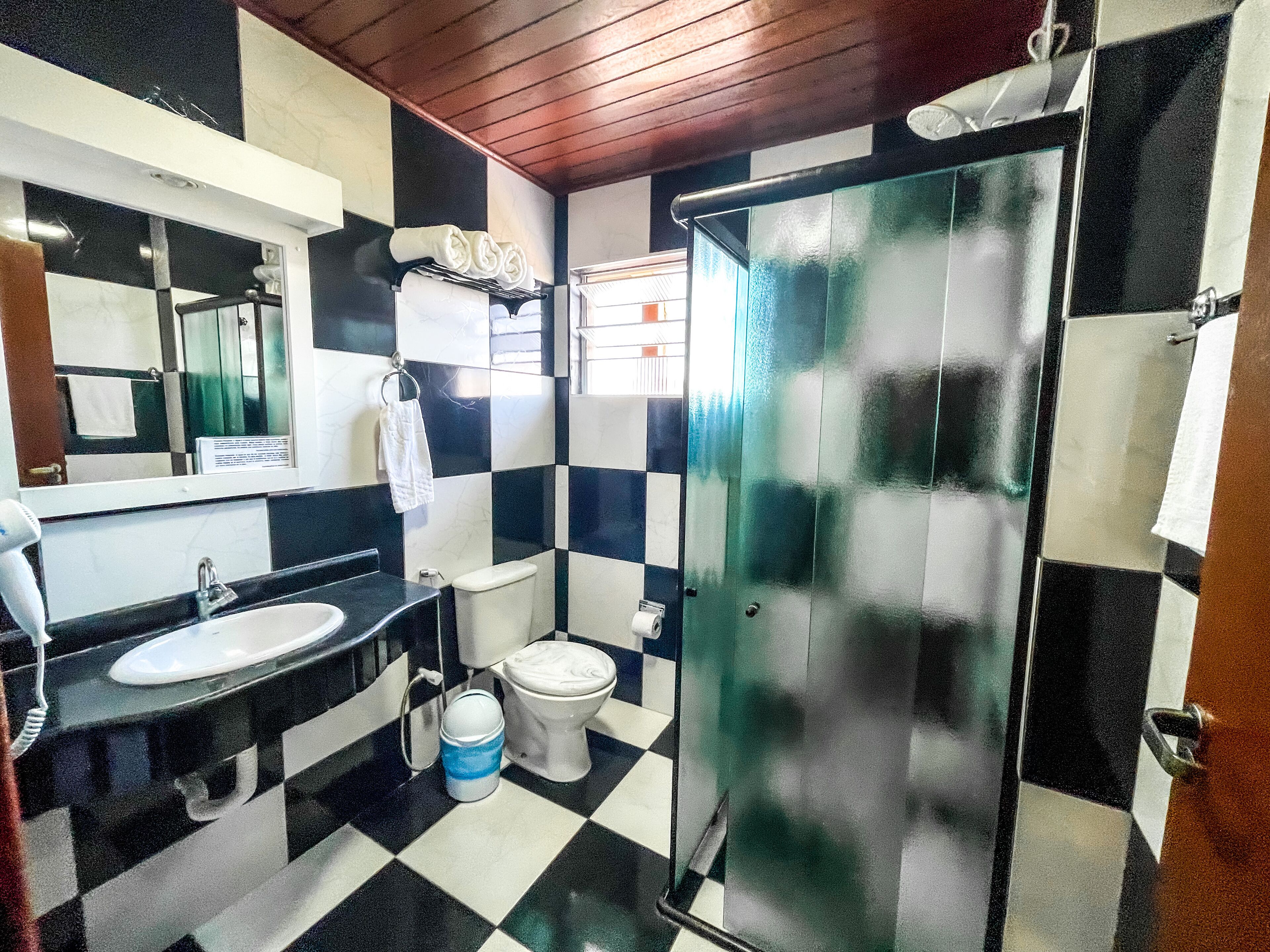 Un baño con suelo a cuadros blanco y negro, un lavabo, un inodoro y una mampara de cristal.
