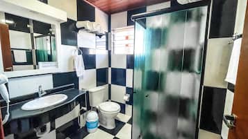 Un baño con suelo a cuadros blanco y negro, un lavabo, un inodoro y una mampara de cristal.