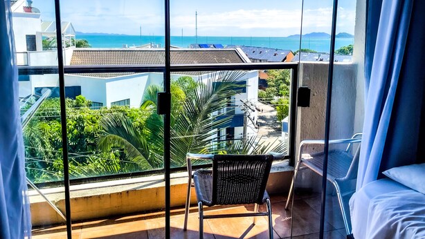 A balcony with a view of the sea and buildings, a chair, and a bed. - Hotel e Pousada Sonho Meu (Florianópolis)