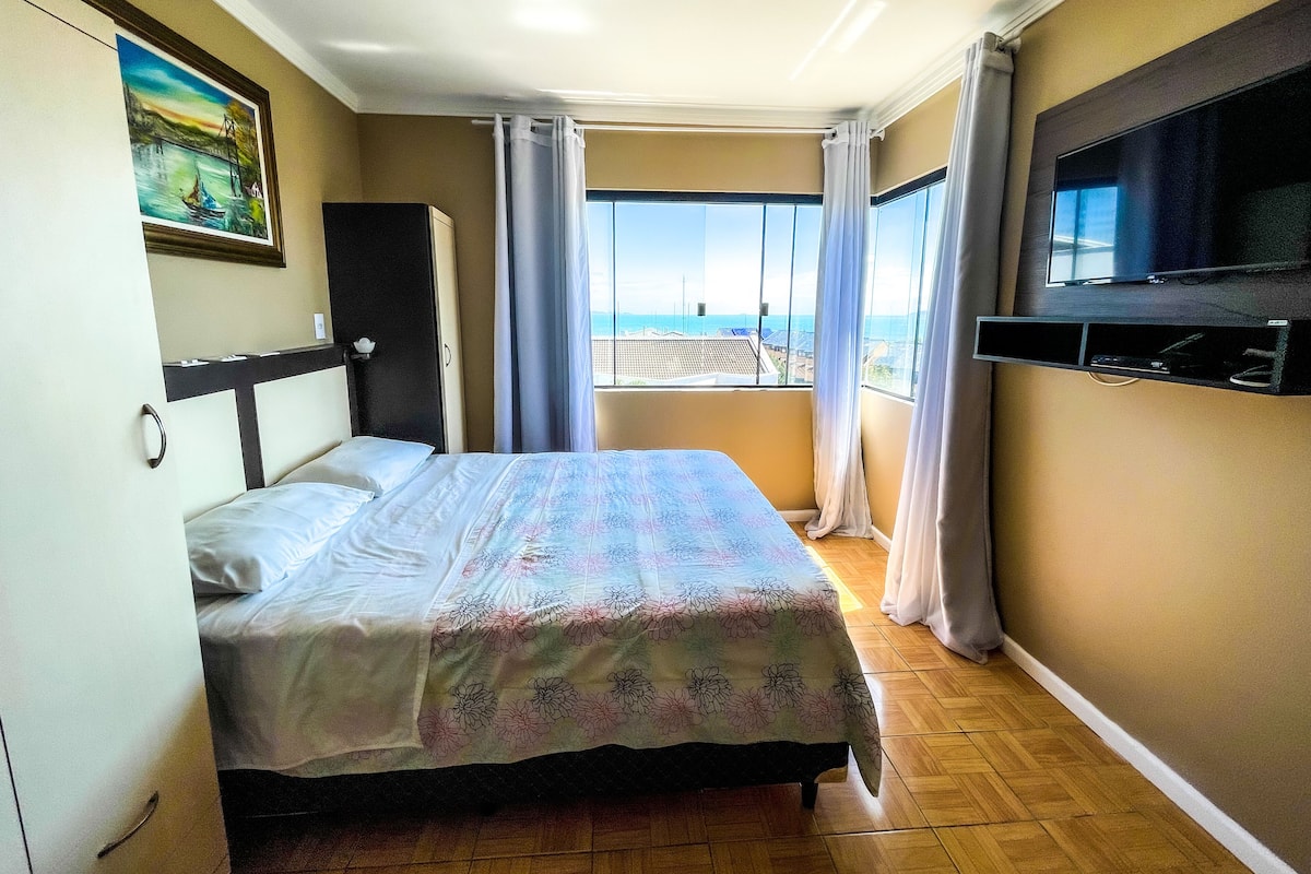 Habitación de hotel con cama, televisión, un cuadro en la pared y vista al mar desde la ventana.