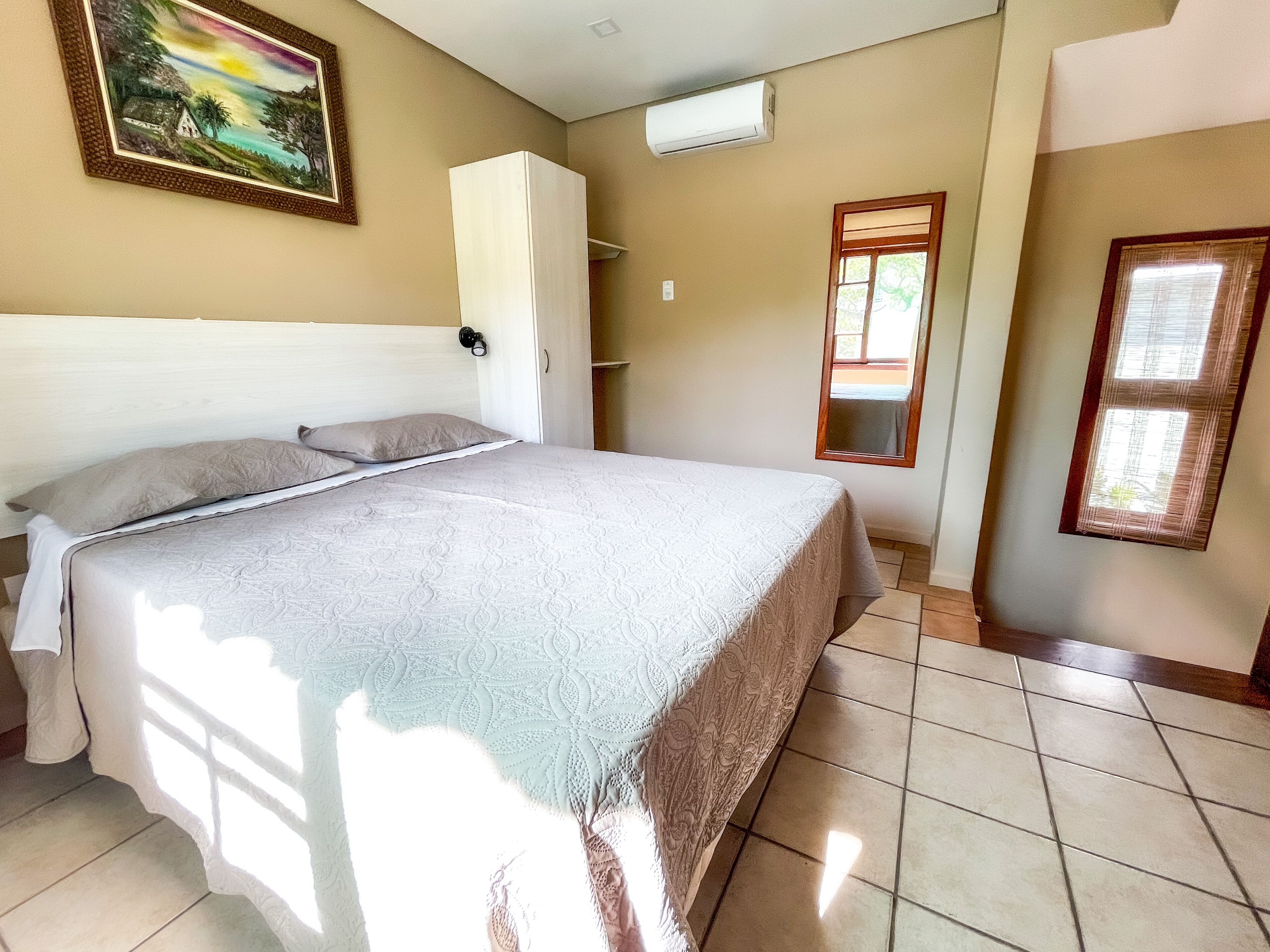 A bedroom with a bed, a wardrobe, a window, and an air conditioning unit.
