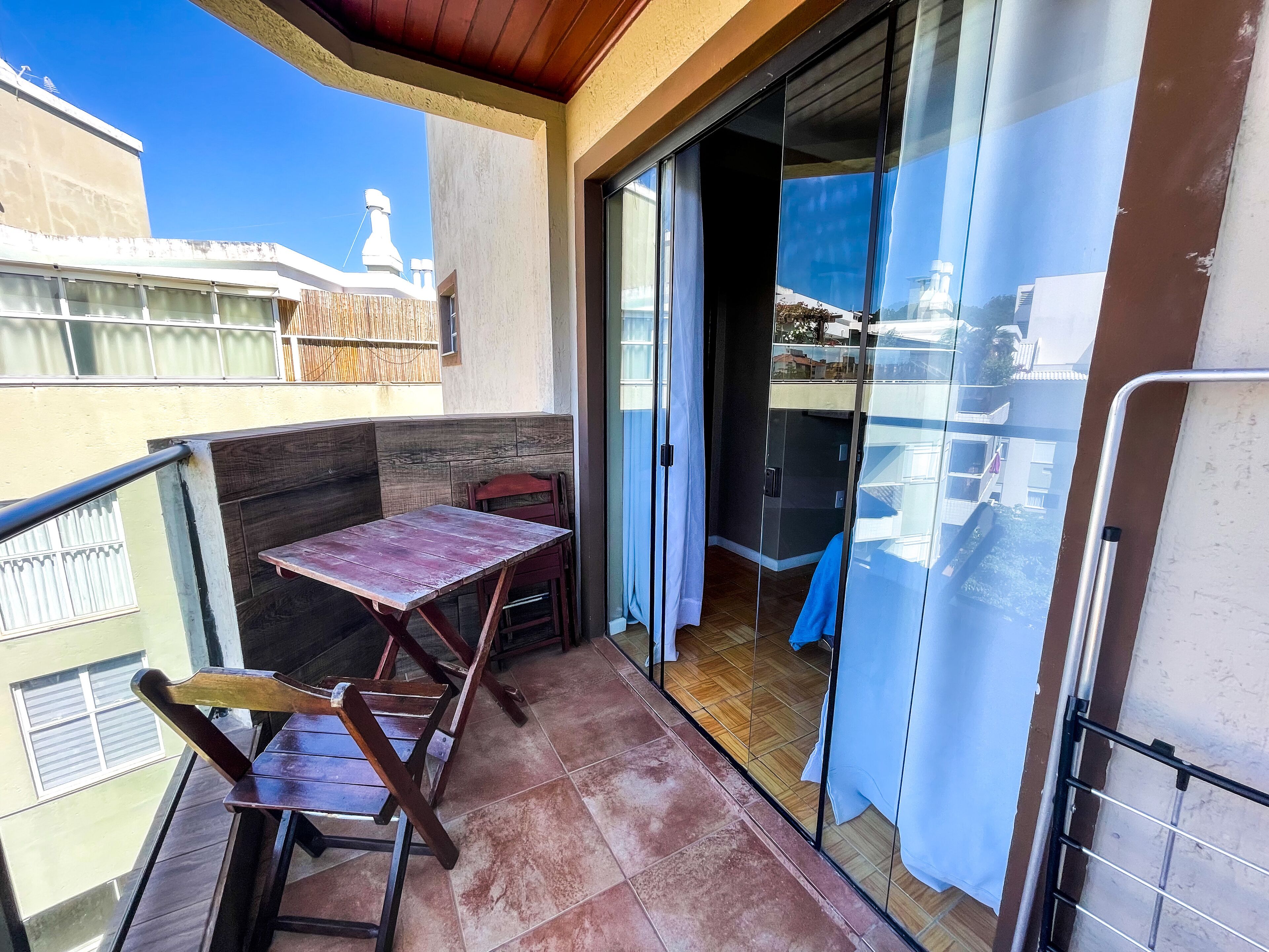 A balcony with a wooden table and chairs, a sliding glass door, and a view of buildings and a tower in the background.
