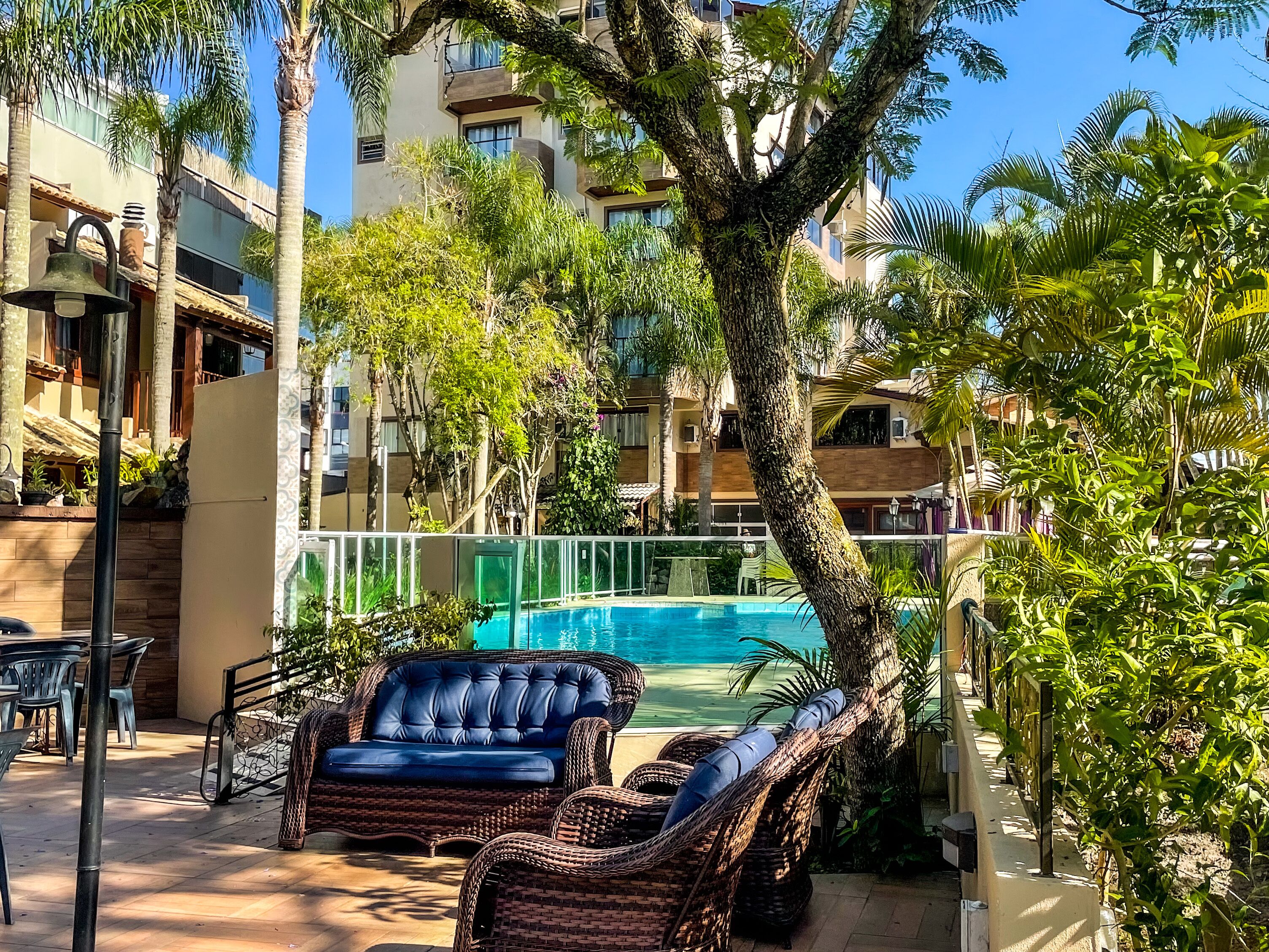Zona de piscina amb mobiliari de vimet, una piscina i vistes a un edifici de diversos pisos.