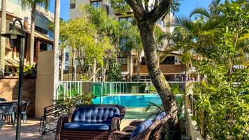 Zona de piscina amb mobiliari de vimet, una piscina i vistes a un edifici de diversos pisos.