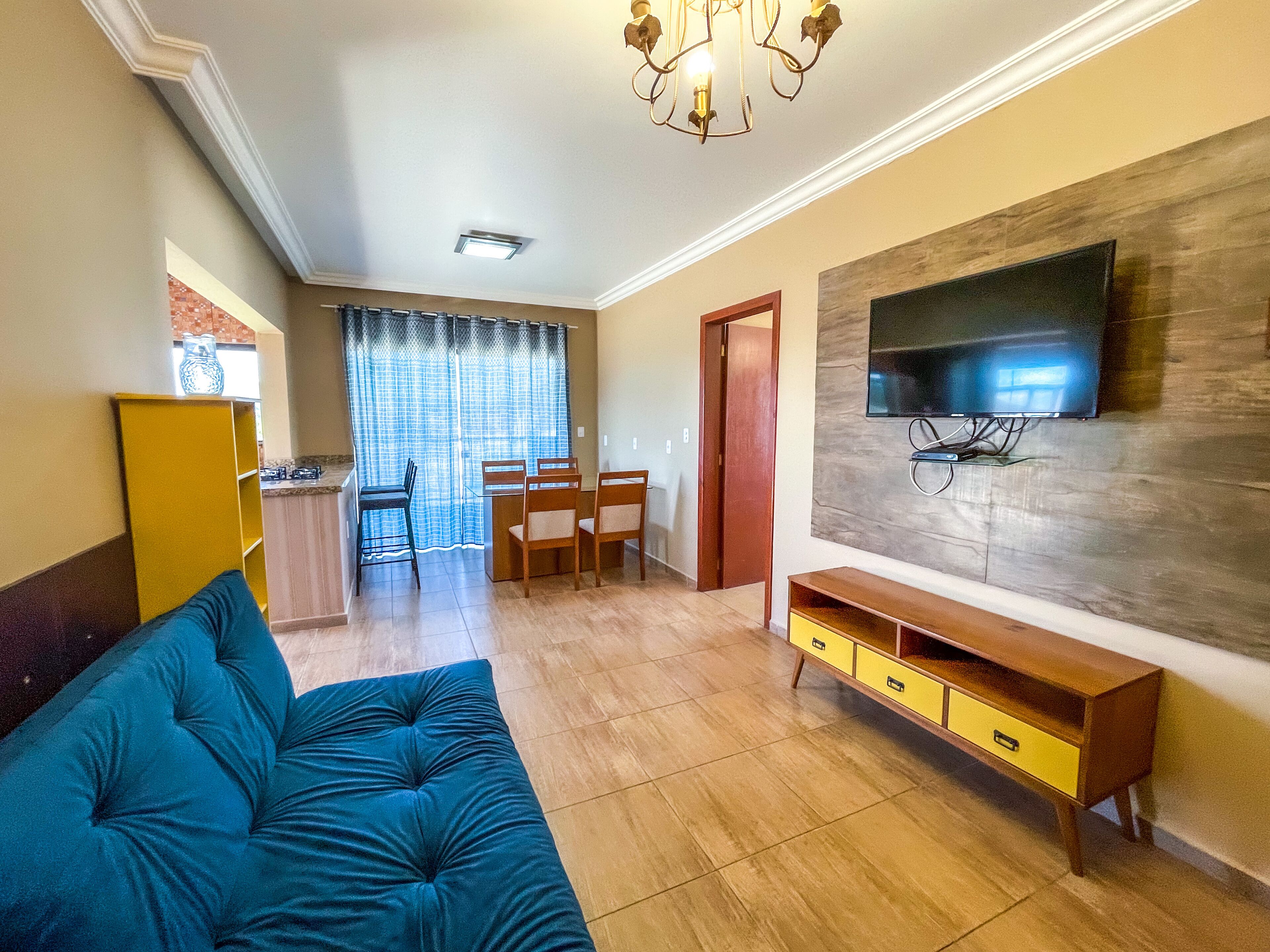 A living room with a blue sofa, a wooden TV stand, and a dining area with a table and chairs.
