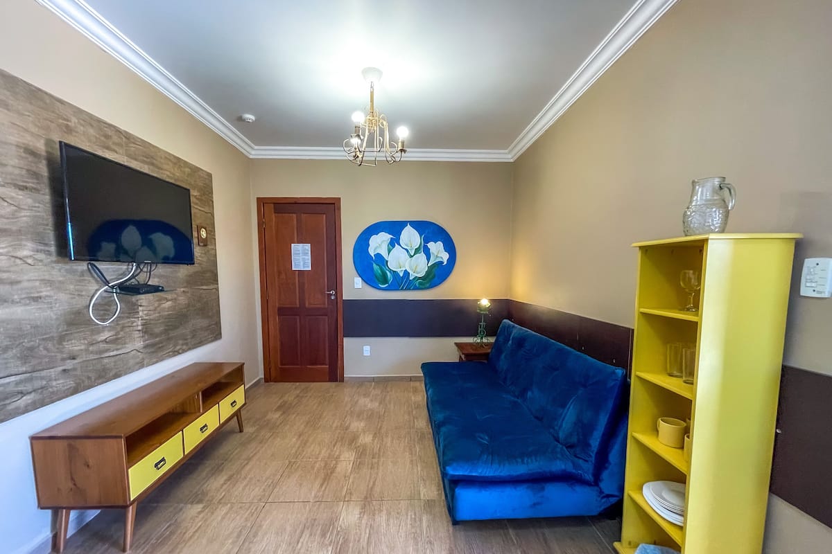 Una sala de estar con un sofá azul, un mueble bajo de madera para el televisor, un estante amarillo y una puerta con un letrero.