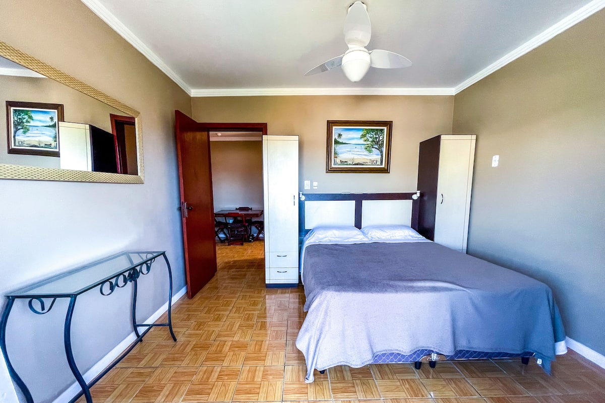 Un dormitorio con una cama, un escritorio y una silla. Hay una puerta que da a otra habitación.