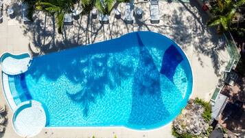 En vy från ovan av en swimmingpool med en kant av kakel, omgiven av solstolar och palmer.