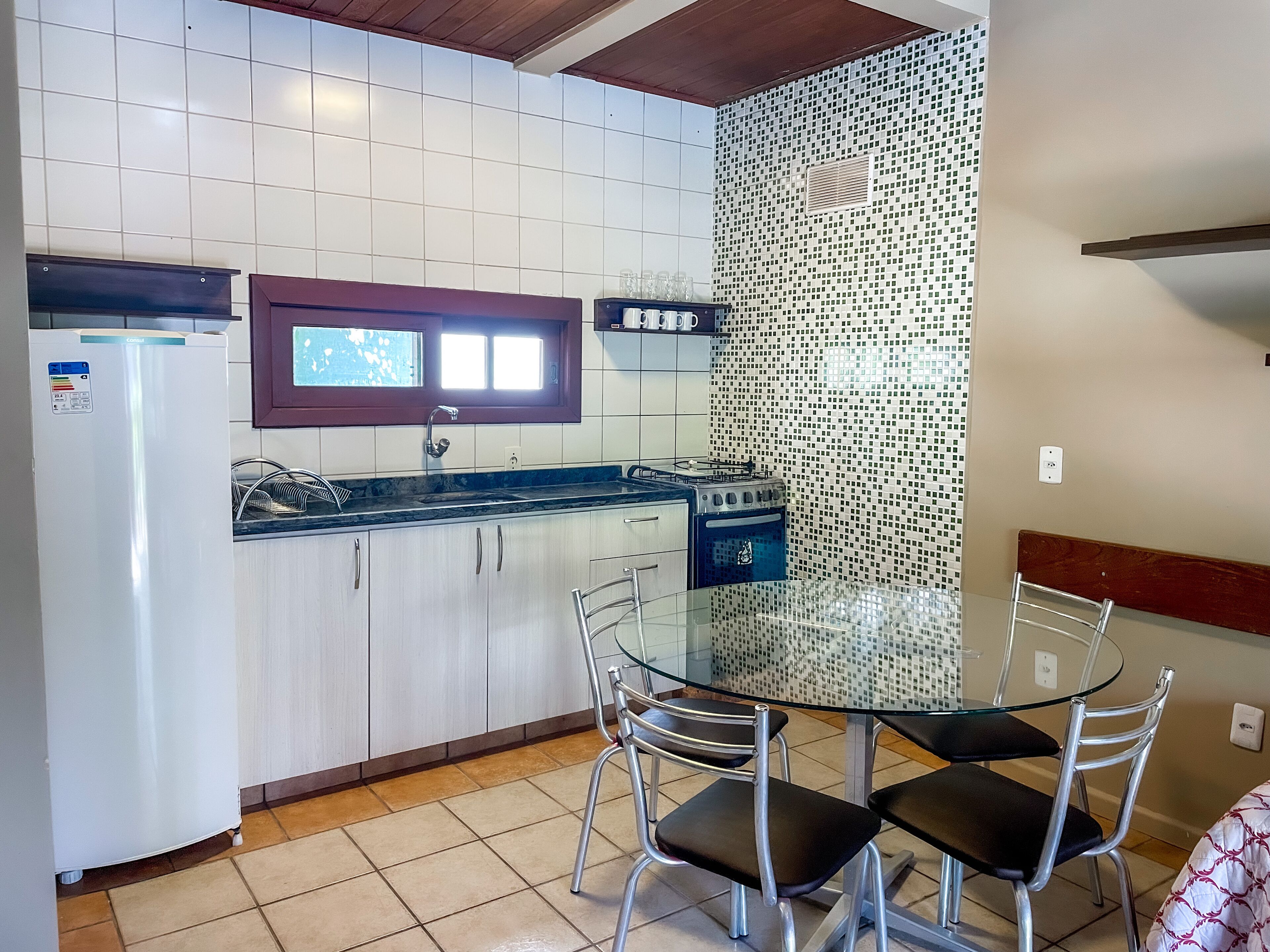 A compact kitchen with white cabinets, a refrigerator, a stove, and a window above the sink.