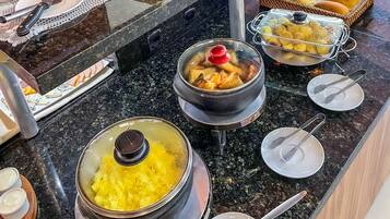 A buffet setup with various dishes, including a pot of soup, a container of yellow food, and a basket of rolls.