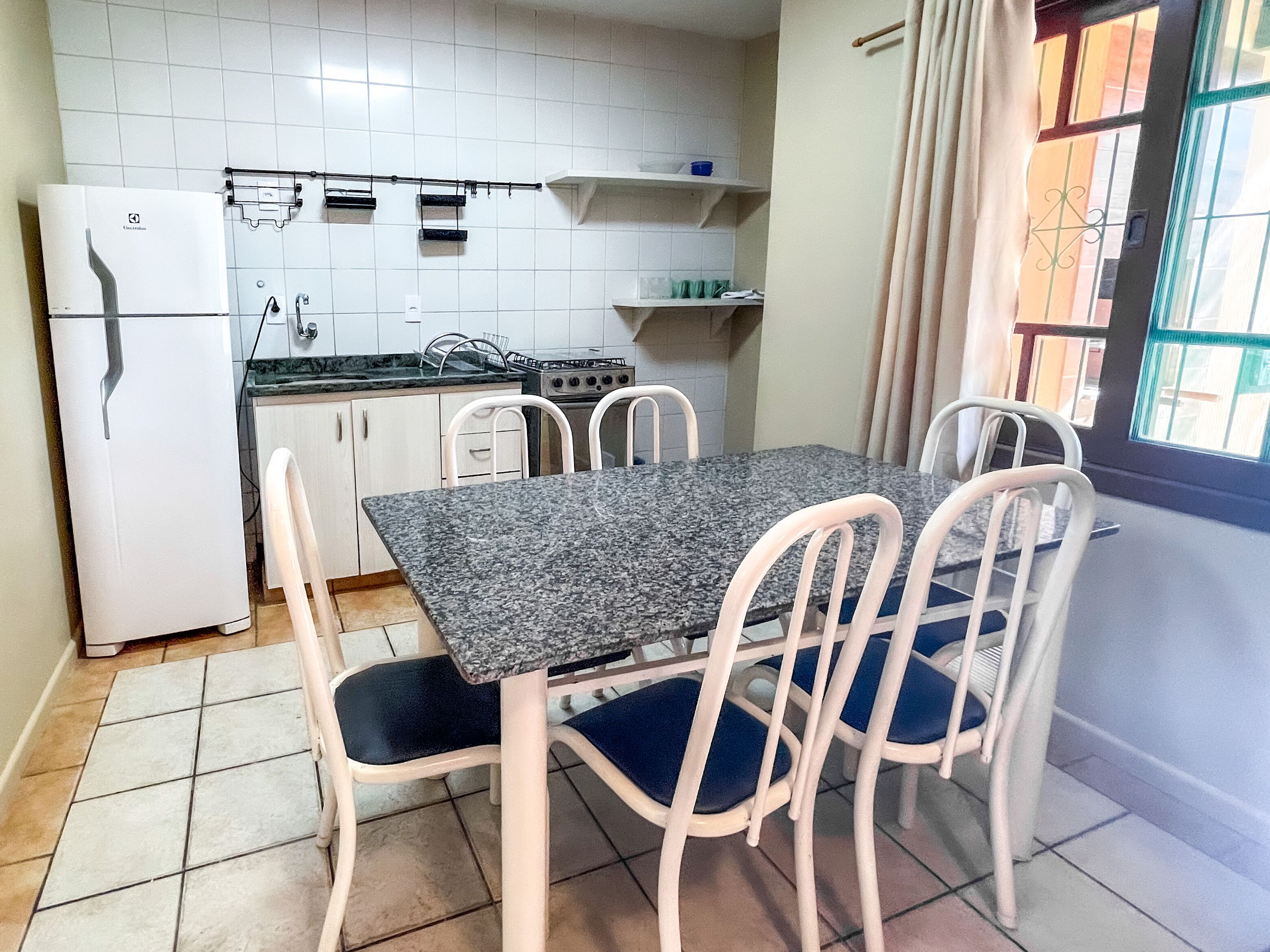 A compact kitchen with white cabinets, a white refrigerator, a gas stove, and a dining table with four chairs.