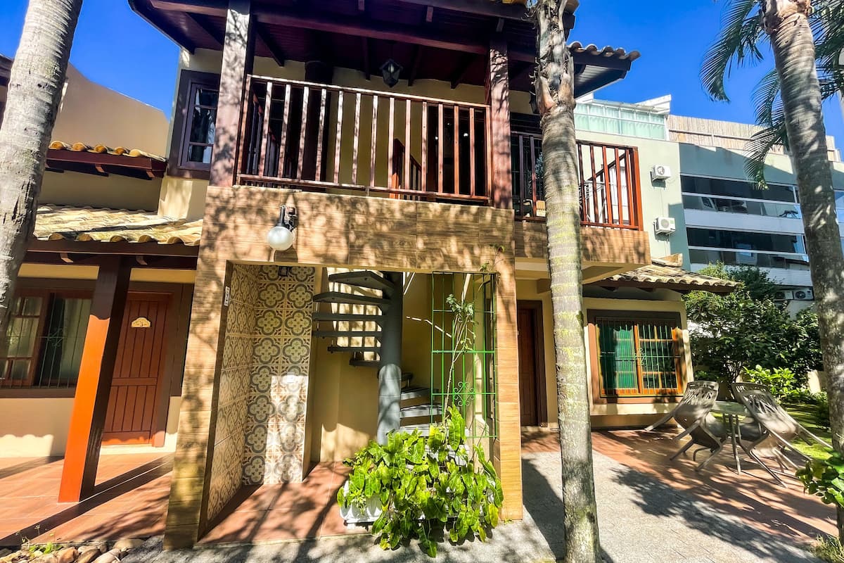 Una casa de dos pisos con un balcón, entrada con tejas y un pequeño jardín.