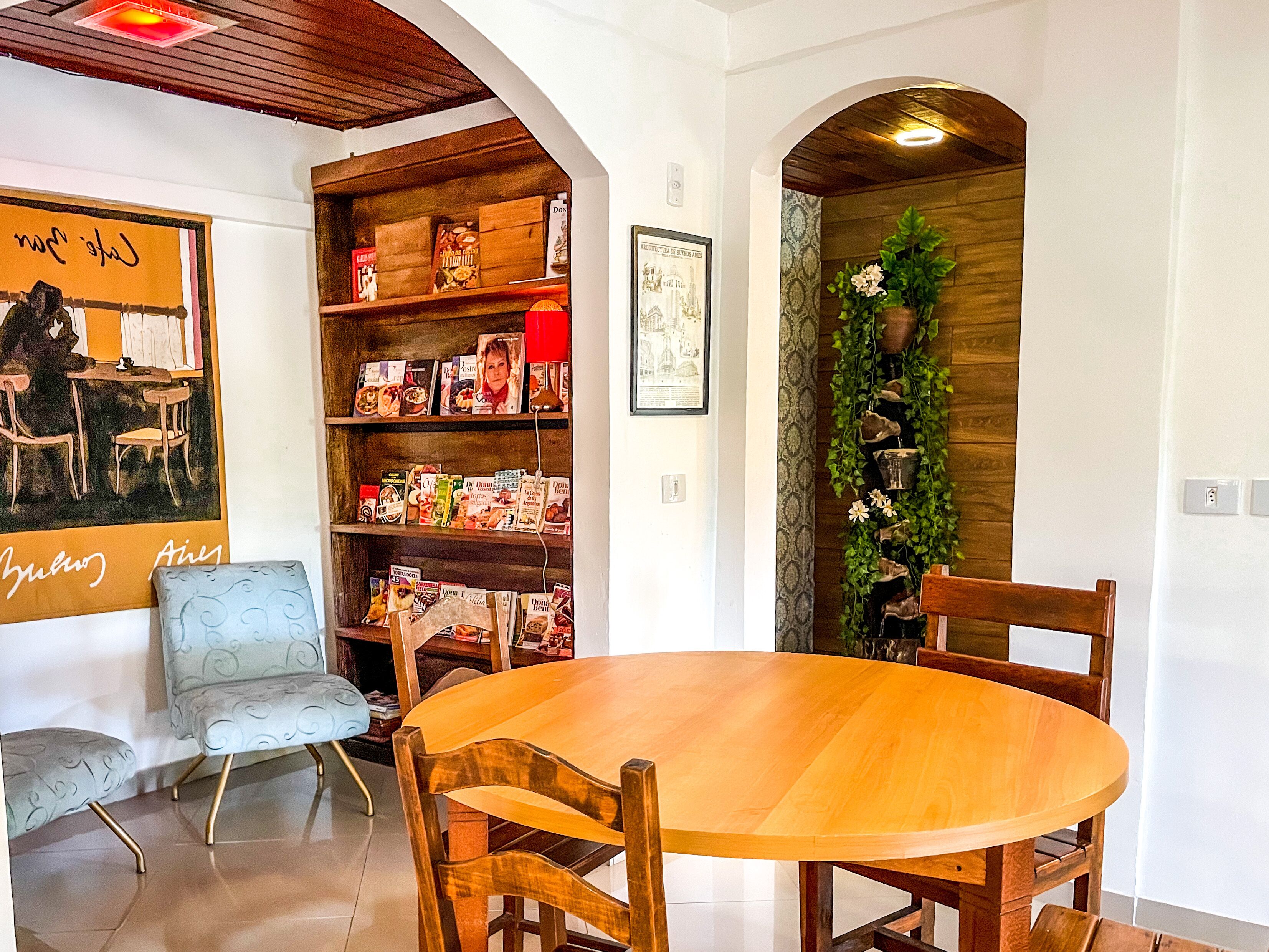 A dining area with a wooden table and chairs, a bookshelf with various items, and a decorative plant.
