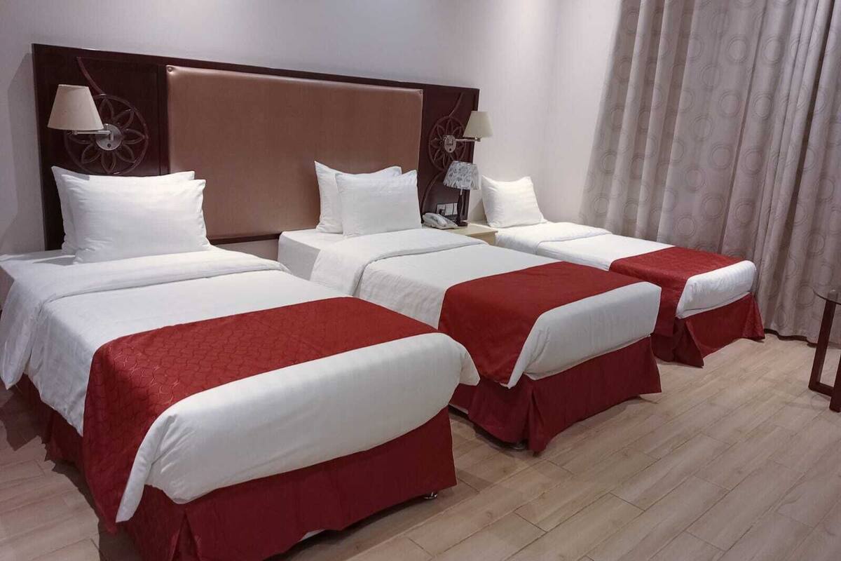 Una habitación de hotel con cuatro camas dispuestas en fila, cada una con ropa de cama blanca y colchas rojas. Hay dos lámparas de pared a cada lado del cabecero.