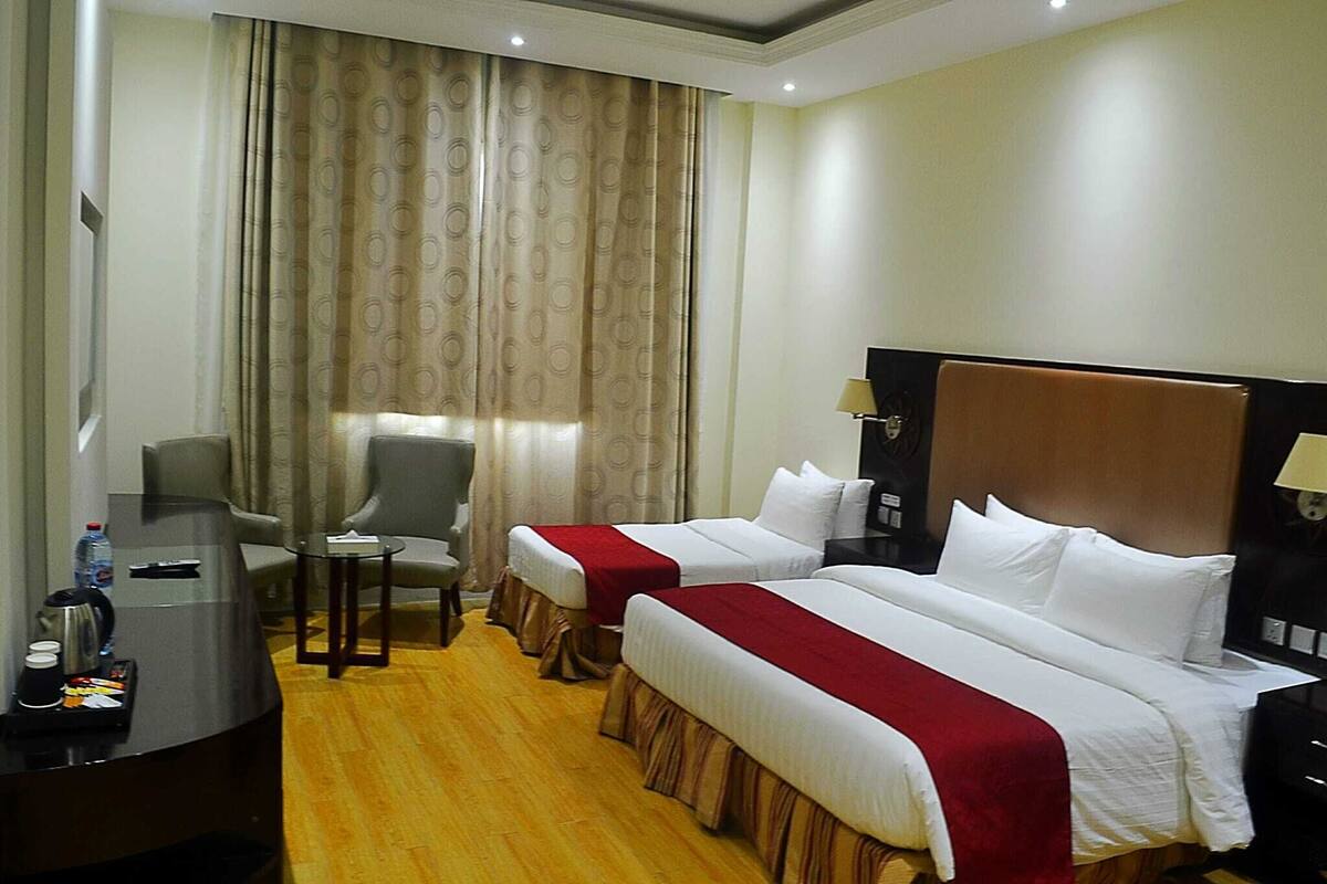 Habitación de hotel con dos camas, un escritorio con silla, una mesita y una ventana con cortinas.