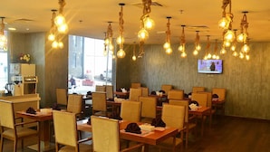 A restaurant with multiple tables and chairs, hanging light fixtures, and a television screen on the wall. - Palm Inn Hotel Doha (Doha)