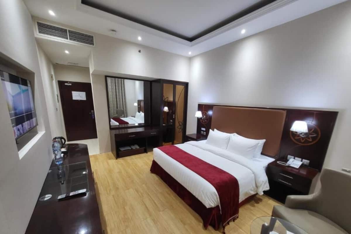 Habitación de hotel con una cama grande, un escritorio, una silla, un televisor y un espejo.