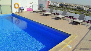 A rooftop pool with clear blue water, surrounded by lounge chairs and a lifebuoy. - Palm Inn Hotel Doha (Doha)