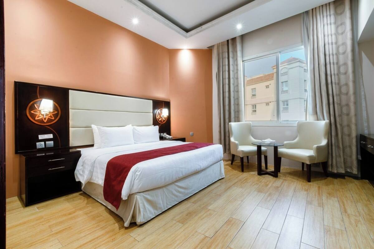 Habitación de hotel con una cama grande, dos sillones, una mesita y una ventana con cortinas.