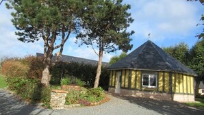 A small, yellow building with a conical roof, surrounded by trees and a garden.