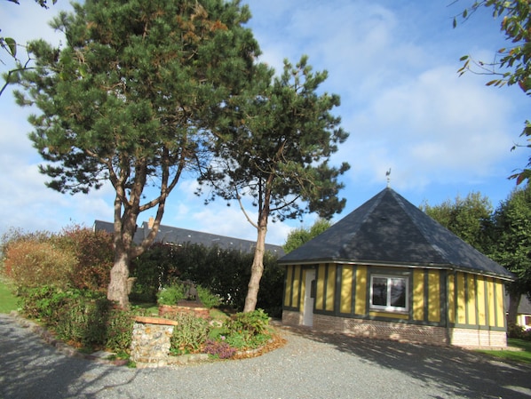 Un petit bâtiment jaune, surmonté d’un toit conique, entouré d’arbres et d’un jardin.