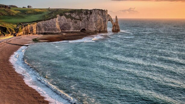 A coastal landscape with a prominent cliff formation and a beach.