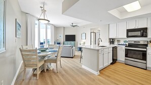 Uma cozinha moderna com armários brancos, uma ilha central e uma área de refeições com cadeiras de madeira e uma mesa de vidro.