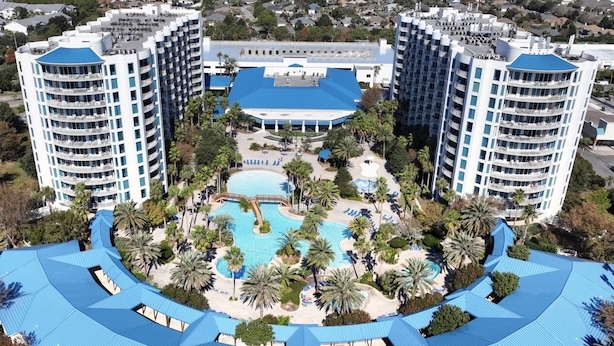 Hotel com piscina central rodeada por palmeiras e um deck com telhado azul.