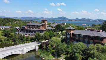 A riverside hotel with a bridge, surrounded by lush greenery and mountains in the background.