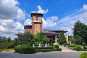A building with a tower, a sign with red text, and a landscaped area with bushes and a fountain. - Haiyi Hotel Xueye (Jinan)