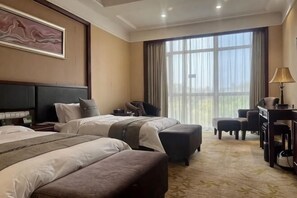 Habitación de hotel con dos camas, un escritorio, una silla, un sofá y un ventanal grande.