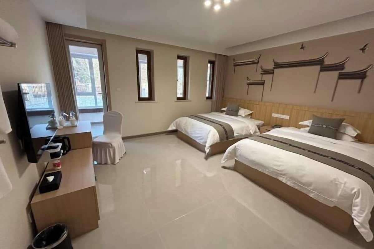 Ein Hotelzimmer mit zwei Betten, einem Schreibtisch mit Stuhl, einem Fernseher und einem großen Fenster.