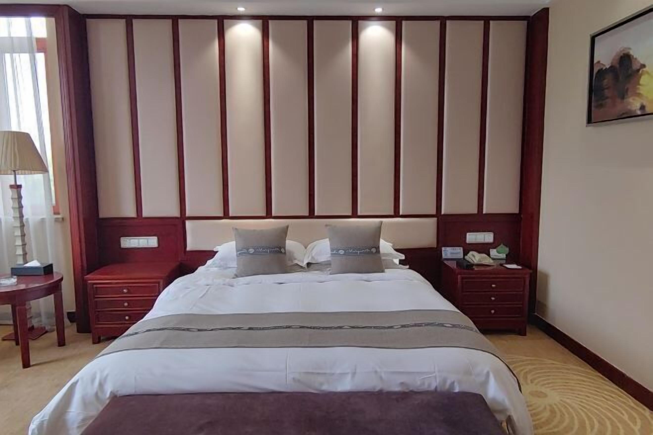 A hotel room with a large bed, two bedside tables, a nightstand, a lamp, and a painting on the wall.