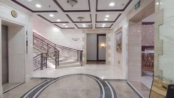 A hotel lobby with a marble floor, a staircase with a metal railing, and a wall-mounted clock.