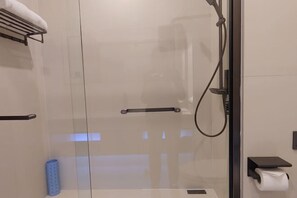 A modern bathroom with a glass shower enclosure, a towel rack, a soap dispenser, and a toilet paper holder. - Haiyi Hotel Xueye (Jinan)