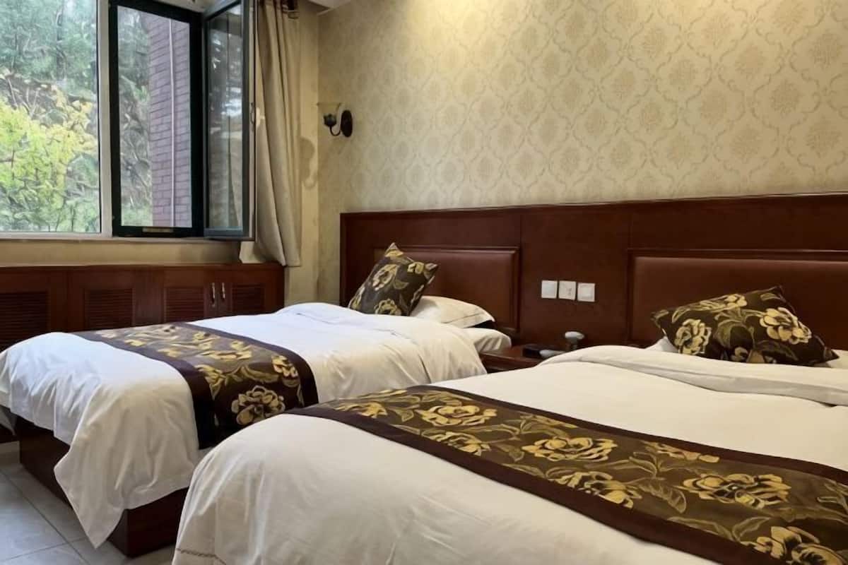 Ein Hotelzimmer mit zwei Betten, einem Fenster mit Vorhängen, einer Wand mit Muster und einem Holz-Kopfteil.