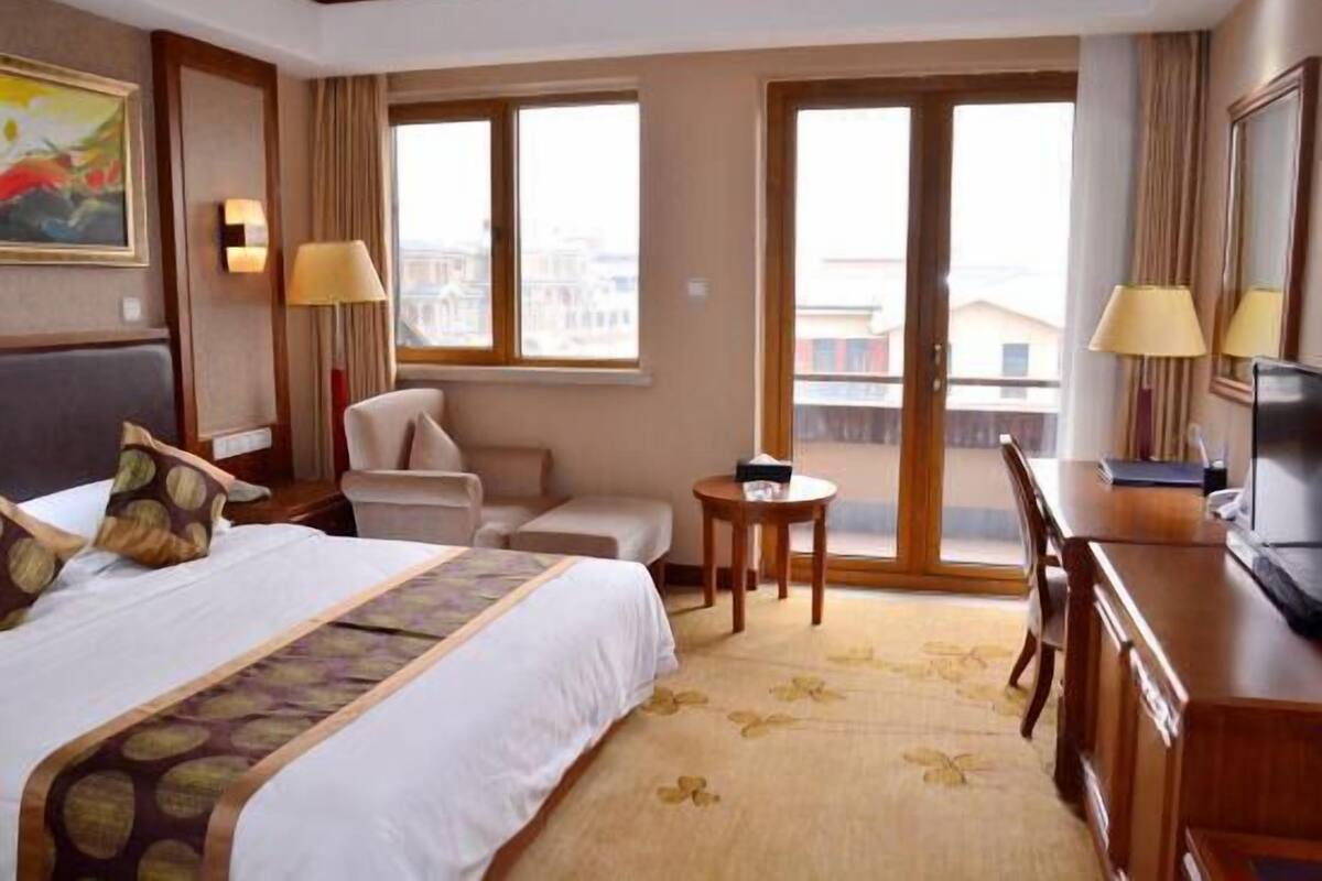 Ein Hotelzimmer mit Bett, Schreibtisch, Stuhl, Fernseher und großen Fenstern.