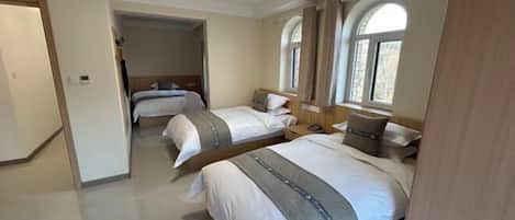 A hotel room with two beds, a wooden headboard, a small desk, and a window with curtains.