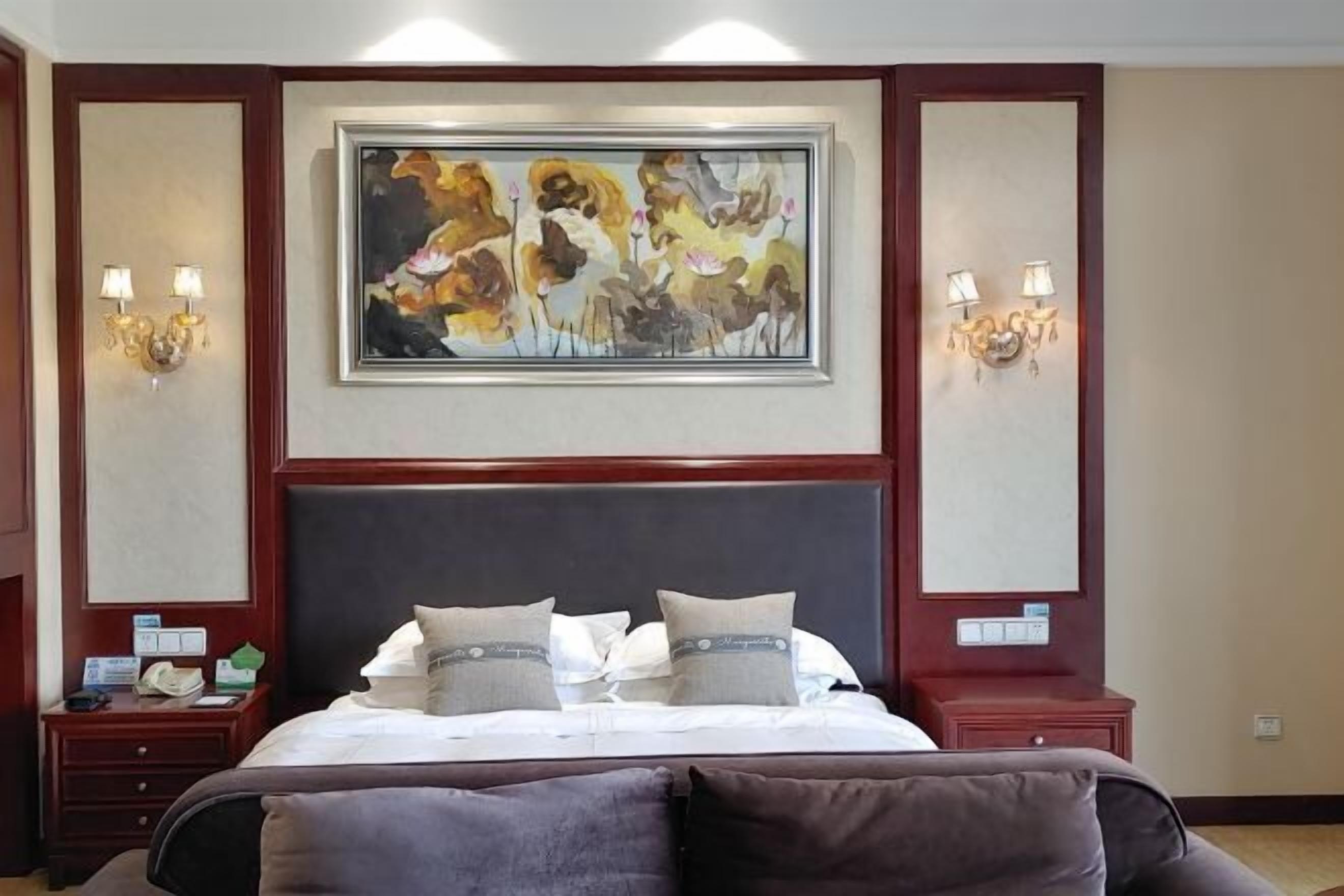 A hotel room with a large bed, two bedside tables, a painting above the bed, and wall sconces.