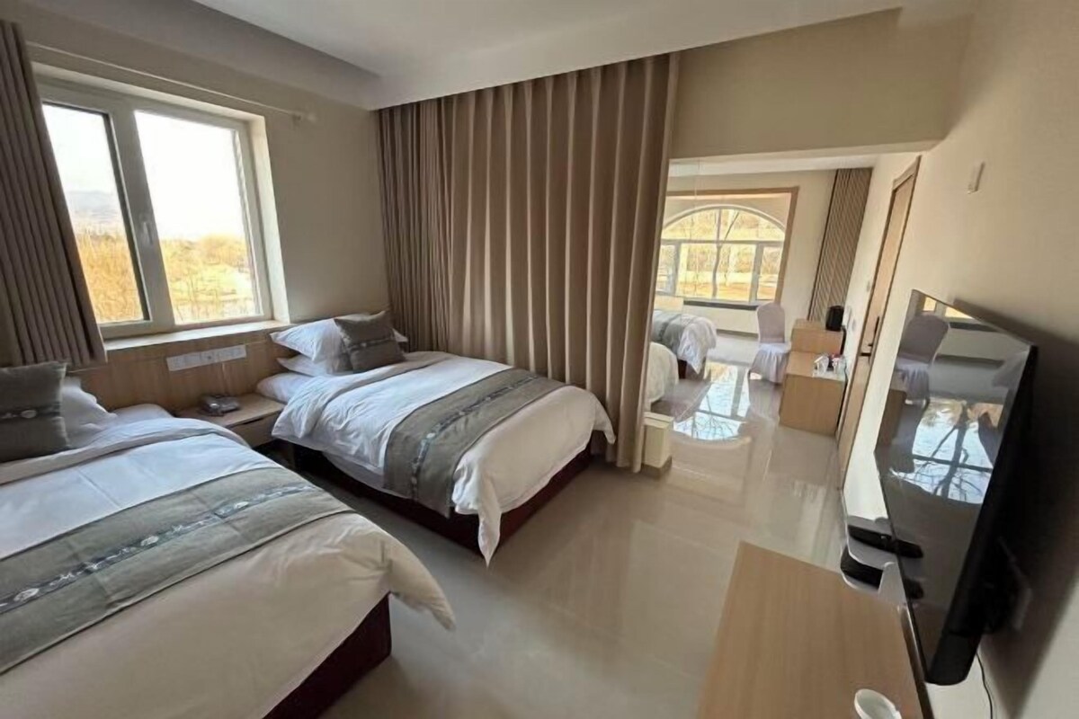 A hotel room with two beds, a TV, a desk, and a view of the outdoors.