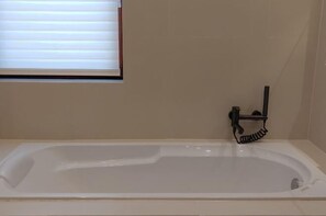 A bathtub with a window above it, a towel rack, and a wall-mounted towel dispenser. - Haiyi Hotel Xueye (Jinan)