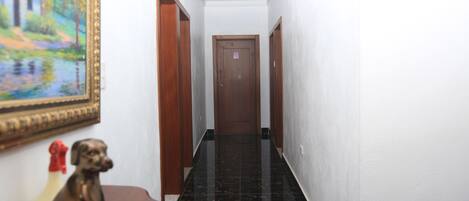 A narrow hallway with a wooden door at the end, white walls, and a black tiled floor.