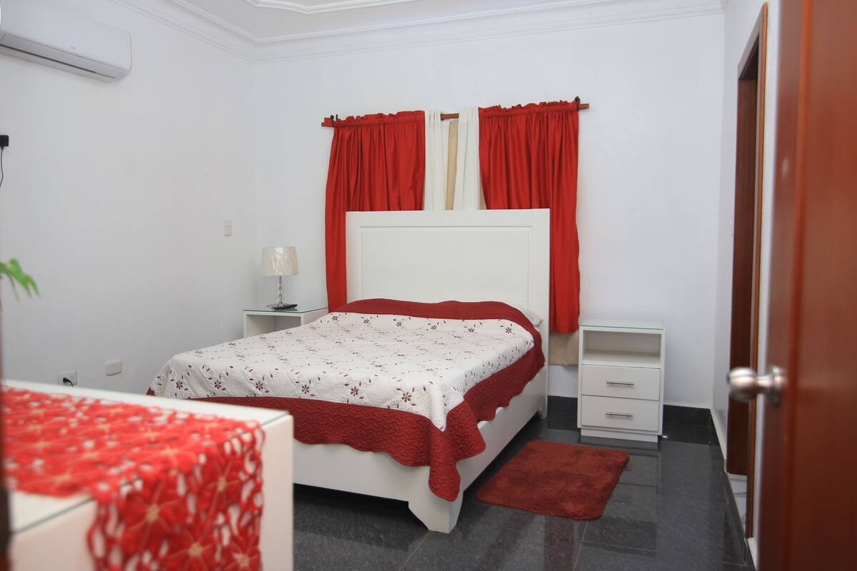 Un dormitorio con cama, mesitas de noche, una lámpara y una alfombra roja.