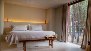A bedroom with a large bed, a bench, and a view of trees through the window.