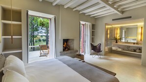 Un dormitorio moderno con una cama grande, chimenea, zona de estar y baño con espejo y estanterías.